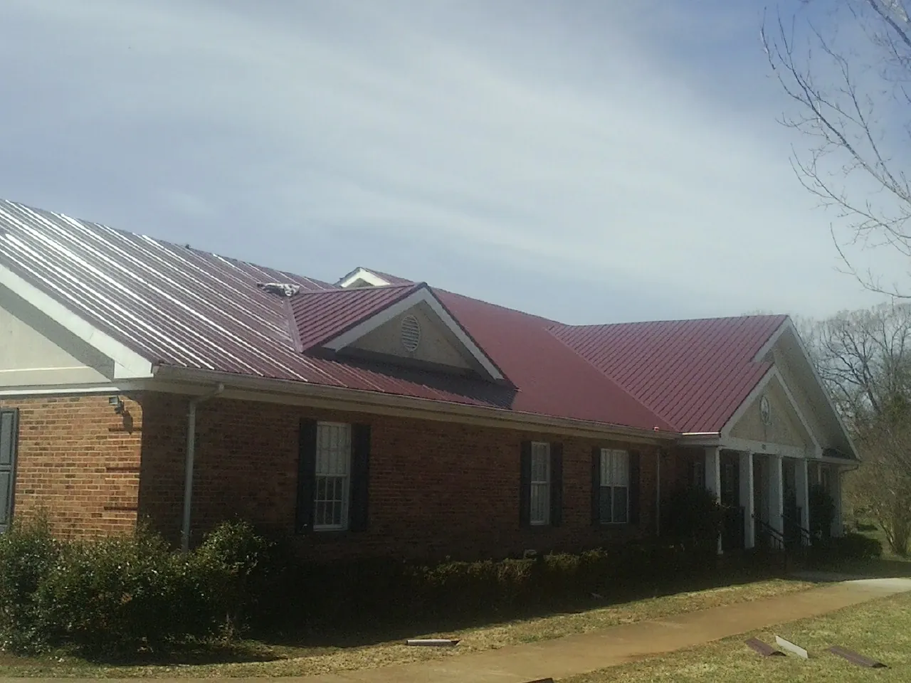 Red metal roof with gabled entries on a long brick building, from a Hail Damage Roof Repair job in Mappsville