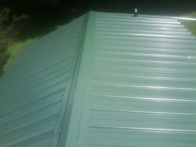 New green metal panels meeting at the ridge of a roof — Flat Roof Repair work by our crew in Mappsville