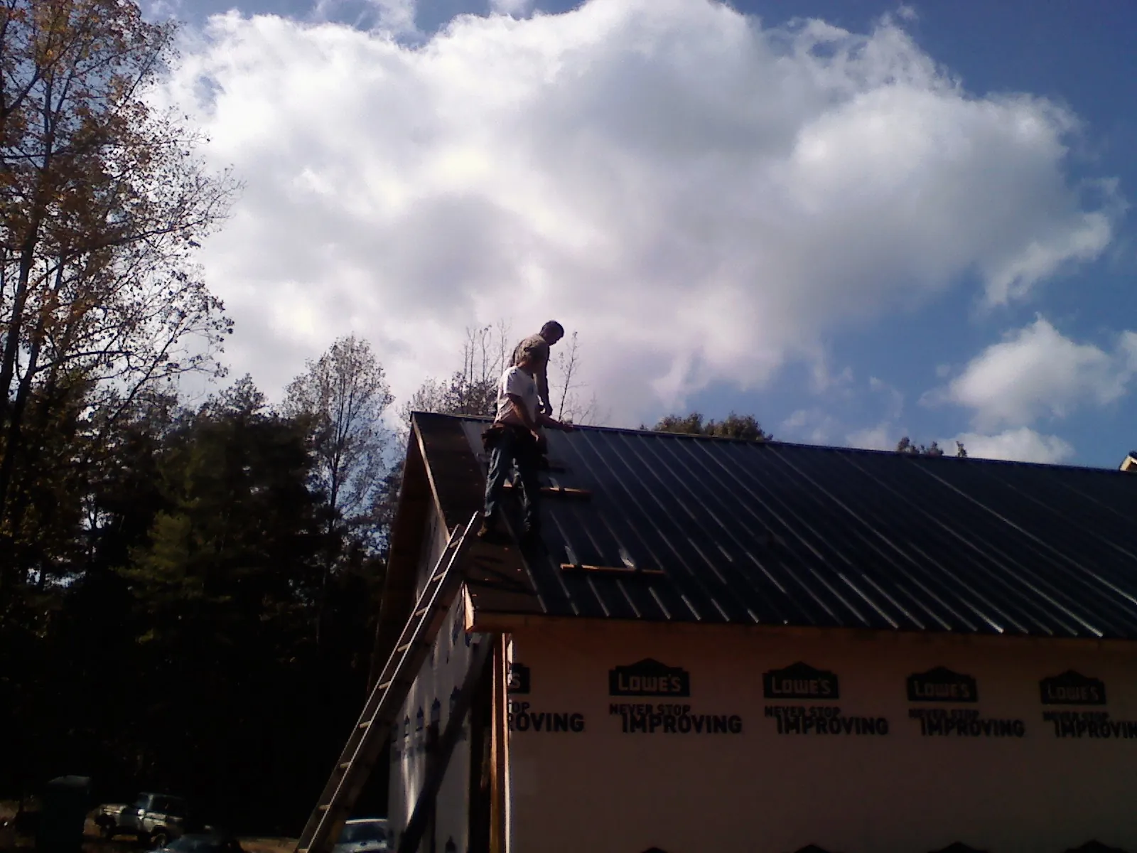 Roofer fastening dark metal panels high against a cloudy sky, from a Roof Inspection job in Mappsville