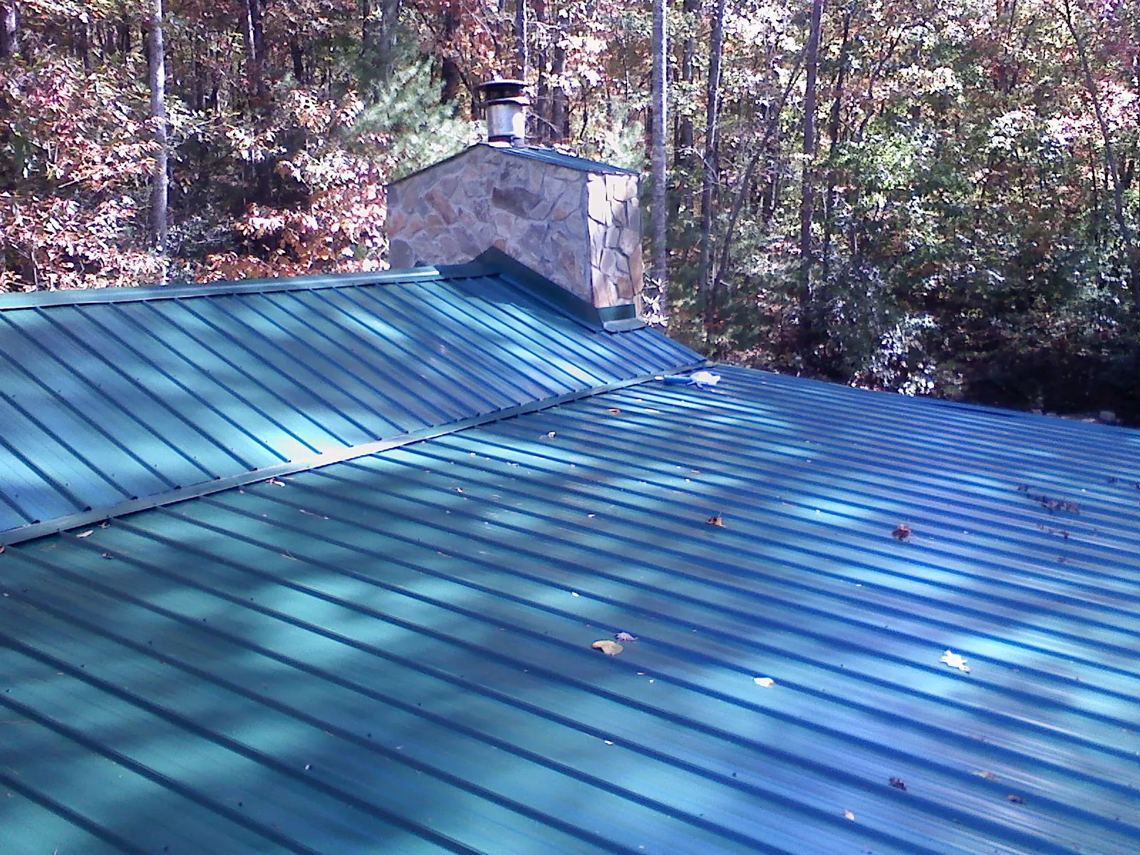 New green metal roof and stone chimney surrounded by autumn woods in Mappsville