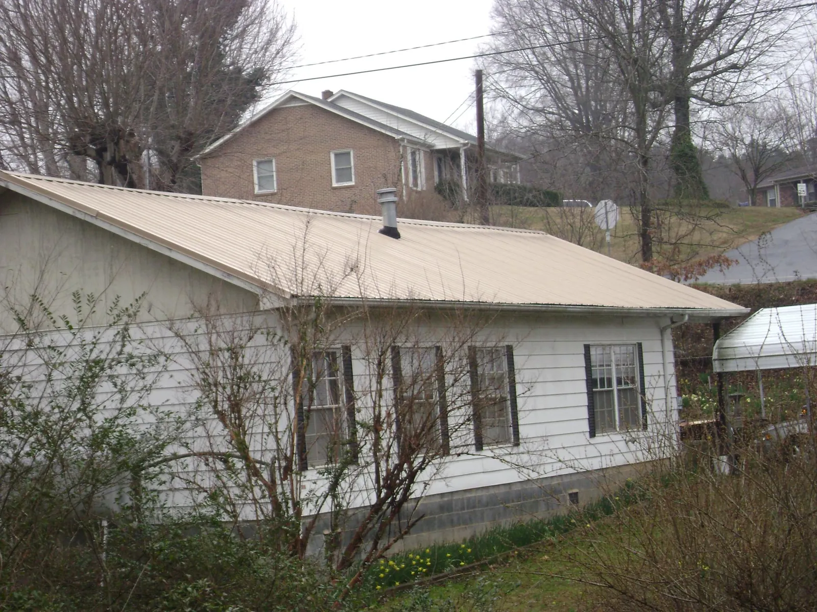 Tan metal roof on a white sided house set into a hillside — Commercial Roofing by Roofing Brothers in Mappsville